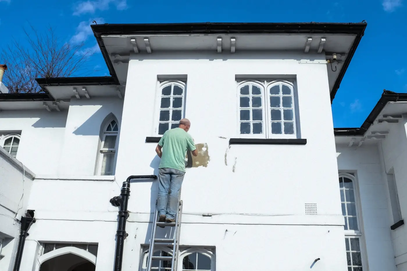 Merdiven üzerinde bir binanın dış cephesini boyayan usta